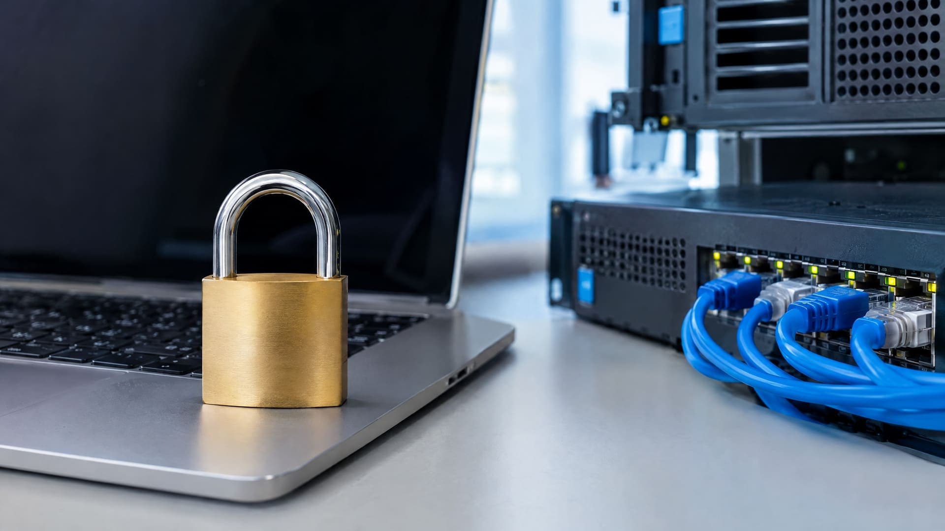 Vorhängeschloss liegt auf einem Laptop neben einem kleinen Server mit Netzwerkkabeln, Symbol für Datenschutz in der Automatisierung, keine Beschriftung