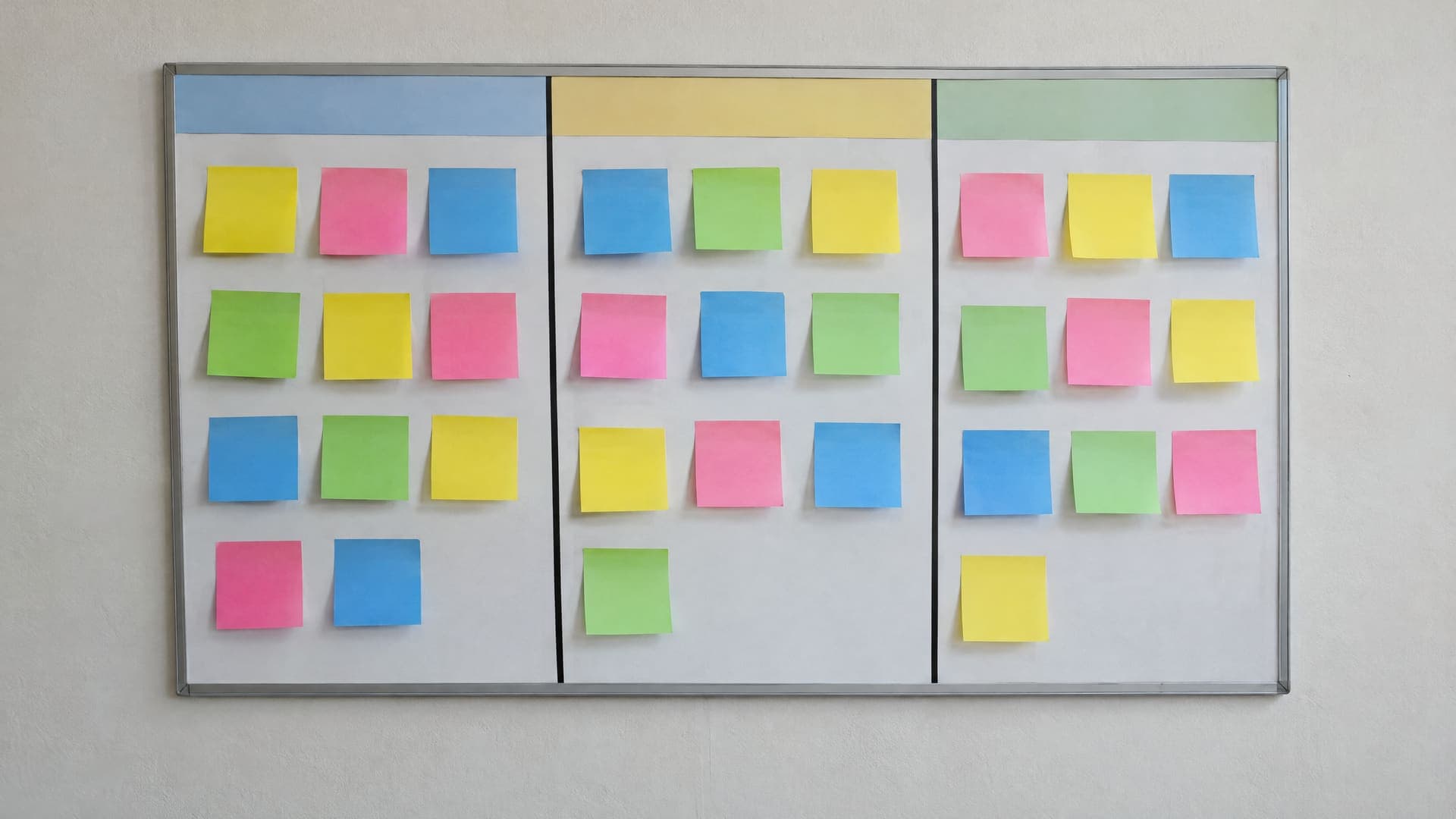 Aufgaben-Board mit Haftnotizen in drei Spalten an einer Wand, keine lesbare Schrift, keine Personen