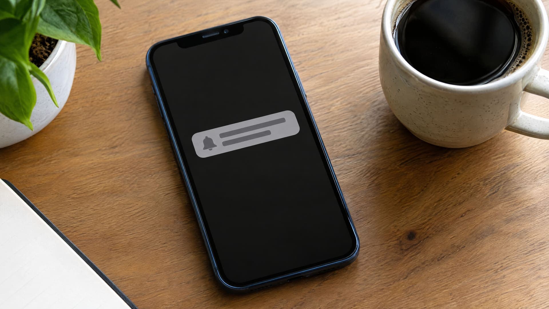 Smartphone zeigt eine Terminerinnerung als Benachrichtigung neben einer Kaffeetasse auf einem Schreibtisch, Text unleserlich
