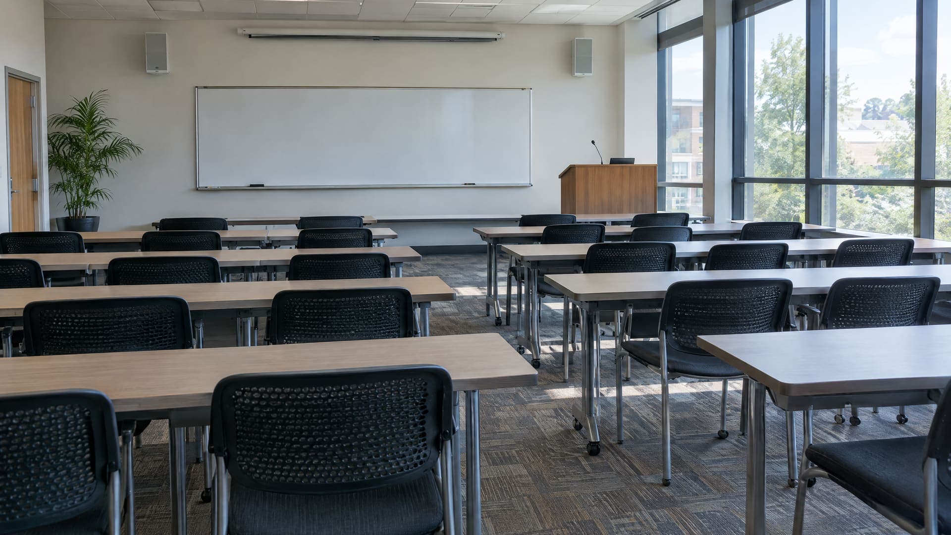 Leerer Seminarraum der Erwachsenenbildung mit Whiteboard, Rednerpult, Tischreihen und Tageslicht durch hohe Fenster