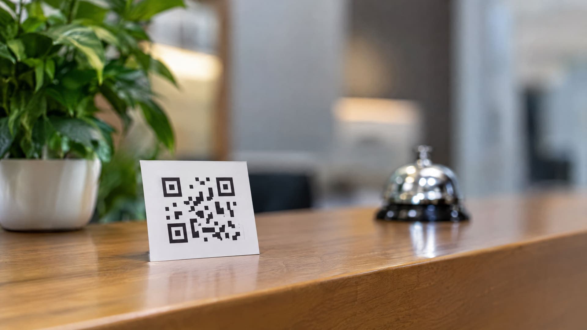 Kleine Karte mit abstraktem QR-Code auf dem Empfangstresen eines Beratungsbüros, im Hintergrund unscharf eine Pflanze und eine Tischklingel, Text unleserlich