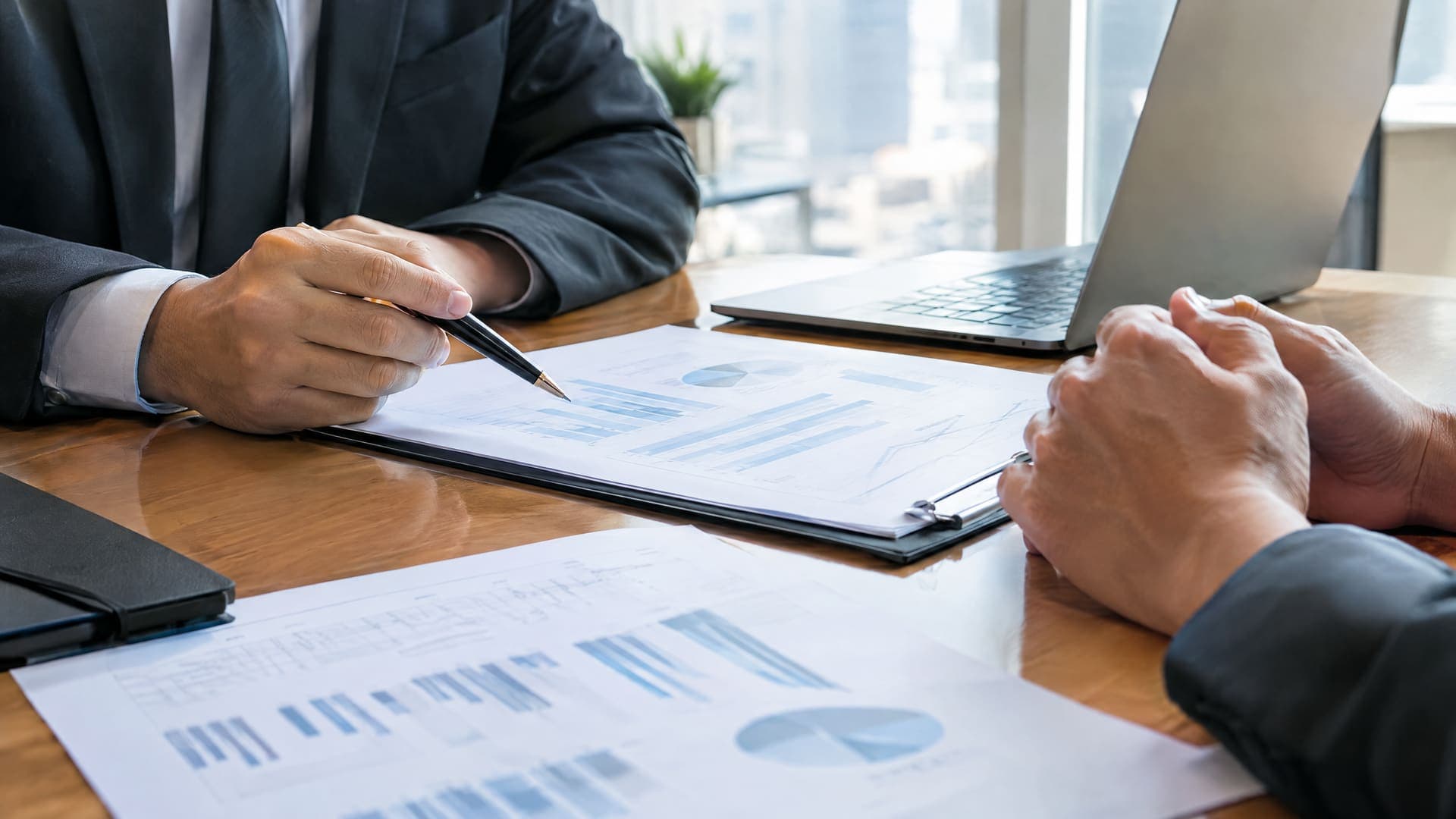 Zwei Hände über einem Tisch mit Unterlagen in einem Investorengespräch, Gesichter nicht sichtbar, Unterlagen unleserlich