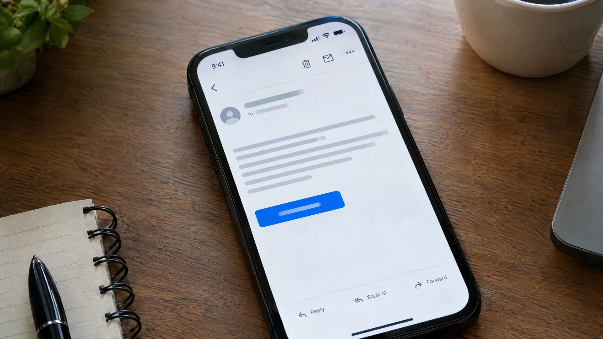 Smartphone zeigt eine E-Mail mit einem Bestätigungs-Button auf einem Schreibtisch, Text unleserlich