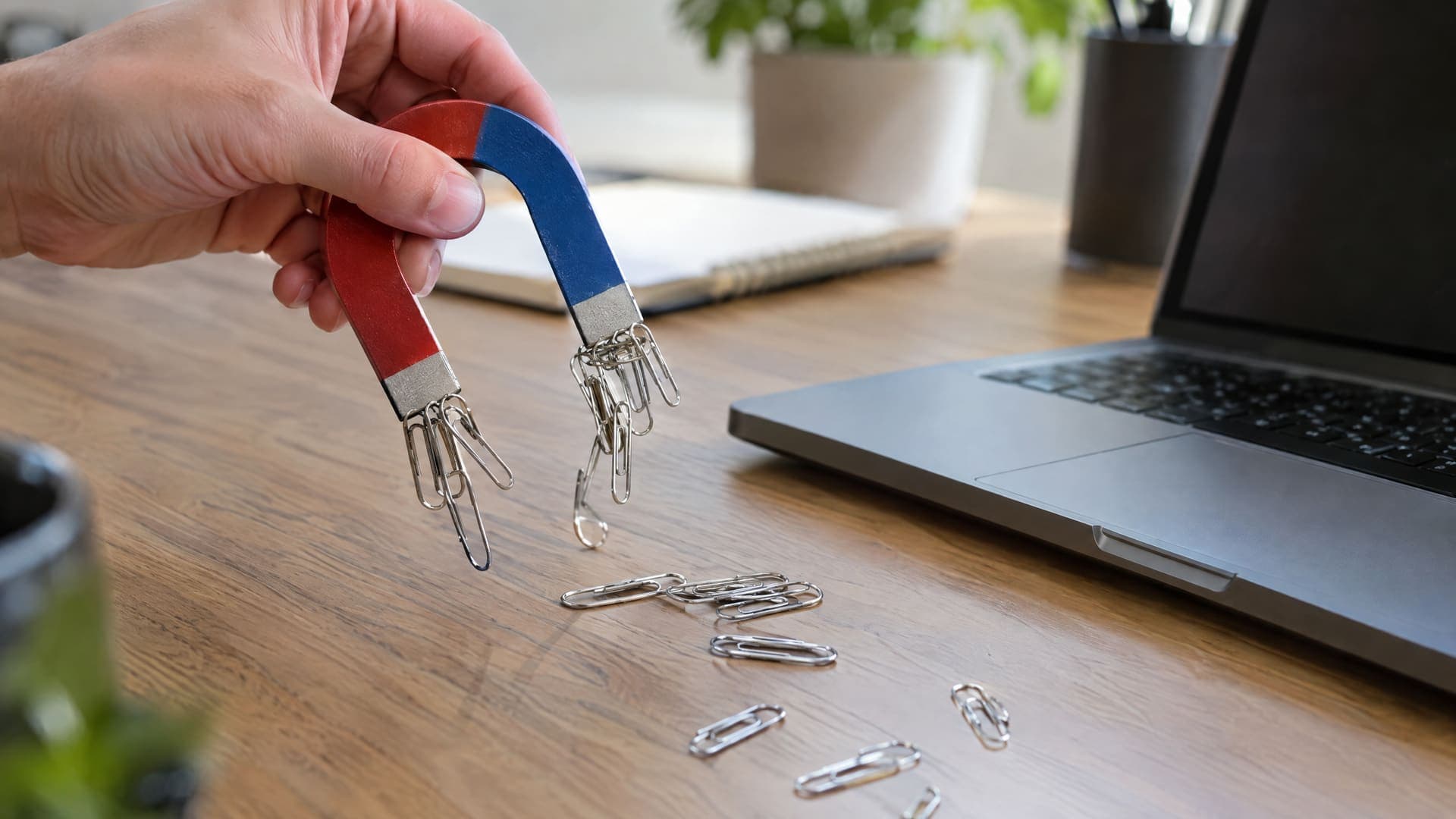 Hufeisenmagnet zieht Büroklammern über einen Schreibtisch neben einem Laptop, geringe Schärfentiefe, keine Beschriftung
