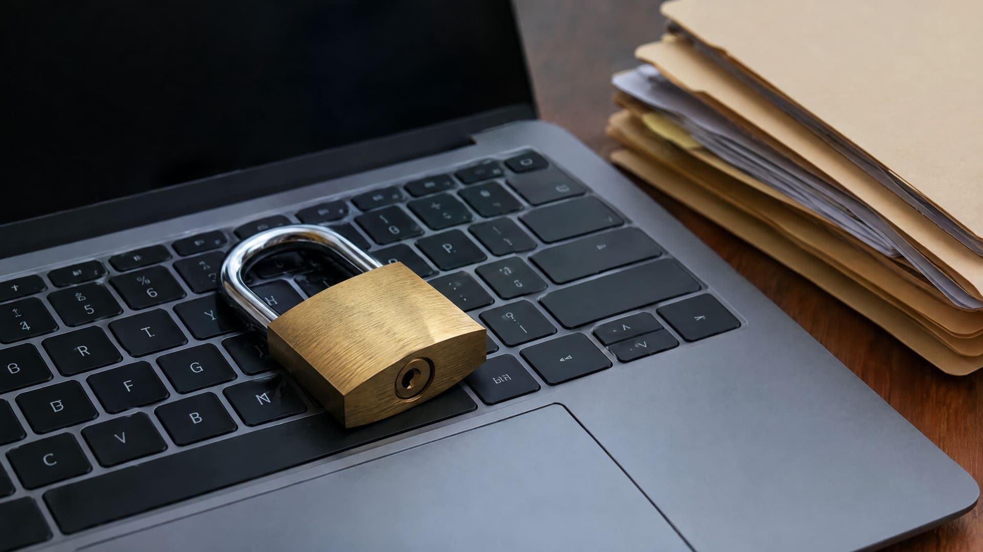 Vorhängeschloss liegt auf einer Laptoptastatur neben einem Stapel Aktenordner als Symbol für Datenschutz, keine Beschriftung