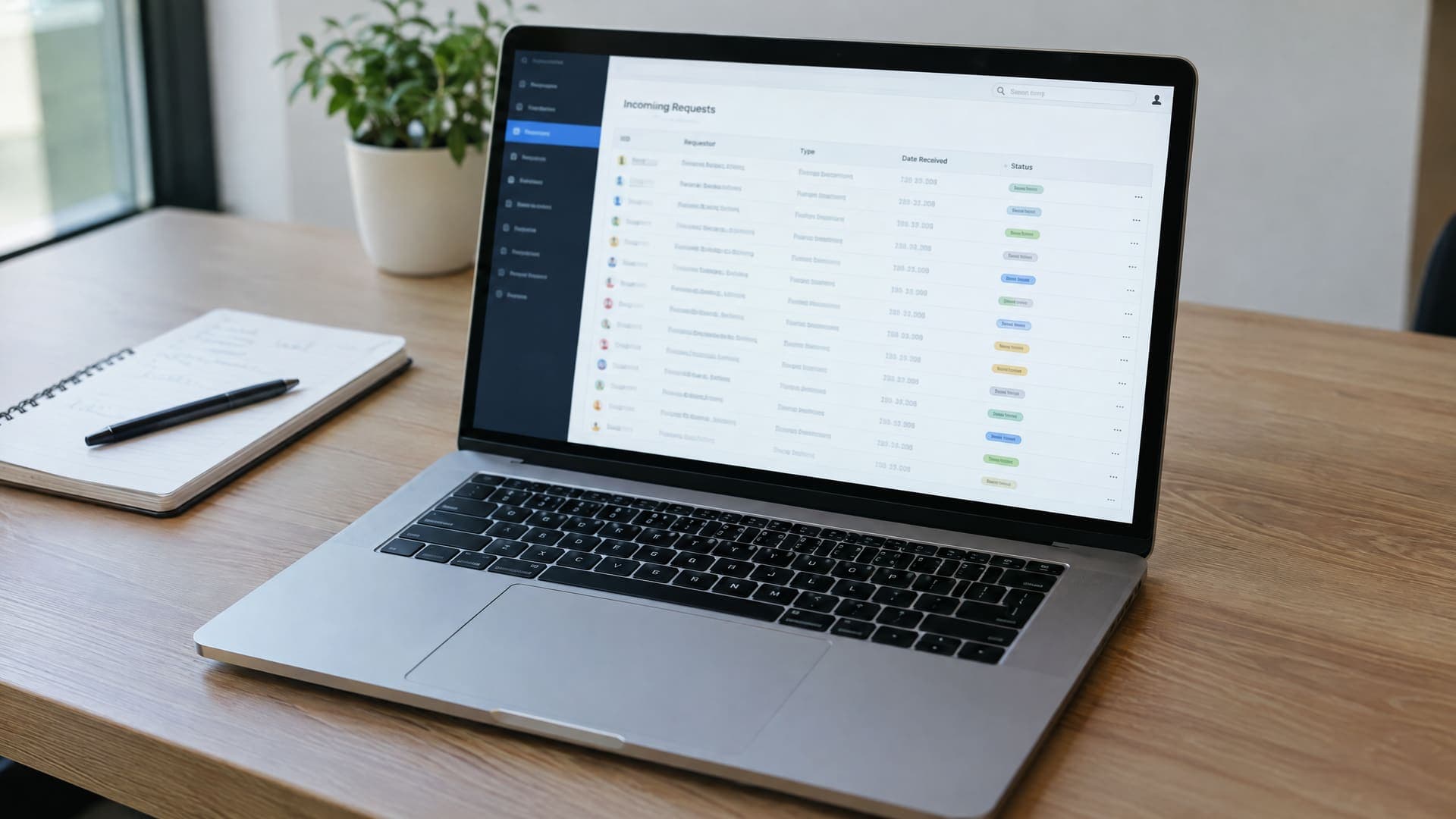 Laptop zeigt eine Portal-Liste eingehender Anfragen in einer Tabelle neben einem Notizbuch, Text unleserlich