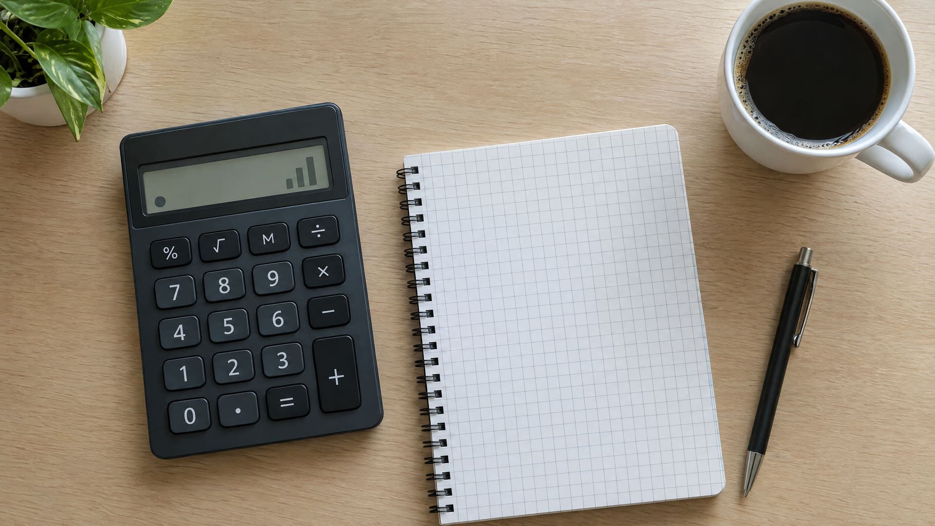 Draufsicht auf einen Taschenrechner mit leerem Display, ein Notizbuch mit Kästchen und eine Kaffeetasse auf einem Schreibtisch, keine Zahlen lesbar