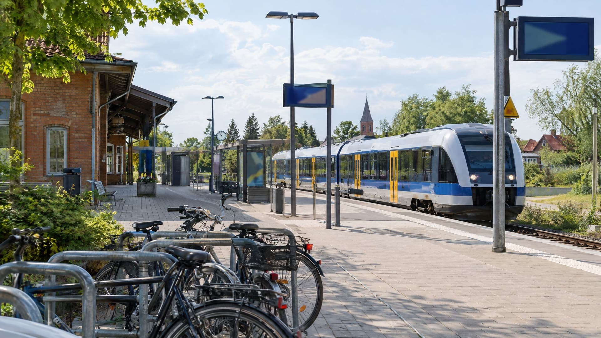 Bahnhofsvorplatz einer Kleinstadt in Brandenburg mit einem Regionalzug und Fahrradständern am Vormittag, ohne erkennbare Personen