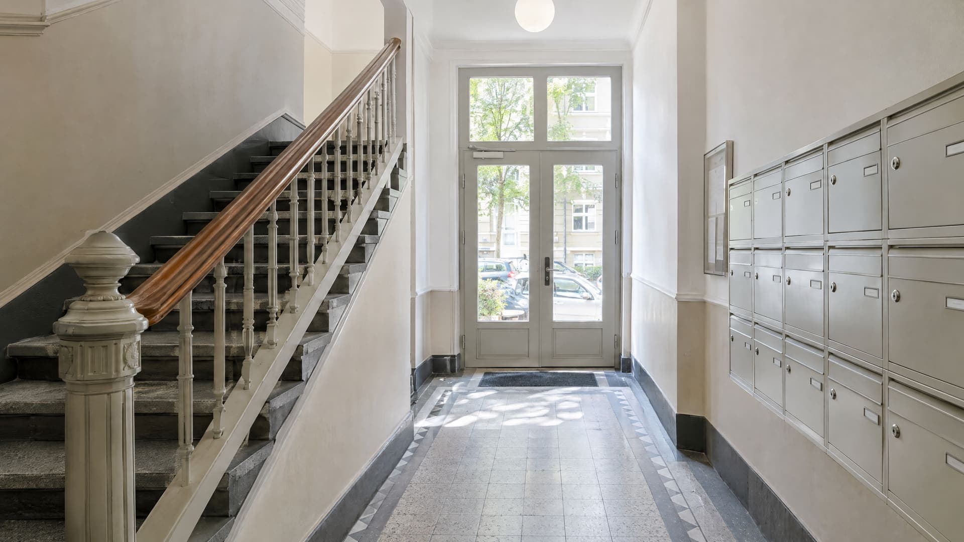 Helles Treppenhaus eines gepflegten Berliner Mehrfamilienhauses mit Geländer und Briefkästen im Eingangsbereich, Namensschilder nicht lesbar, keine Personen
