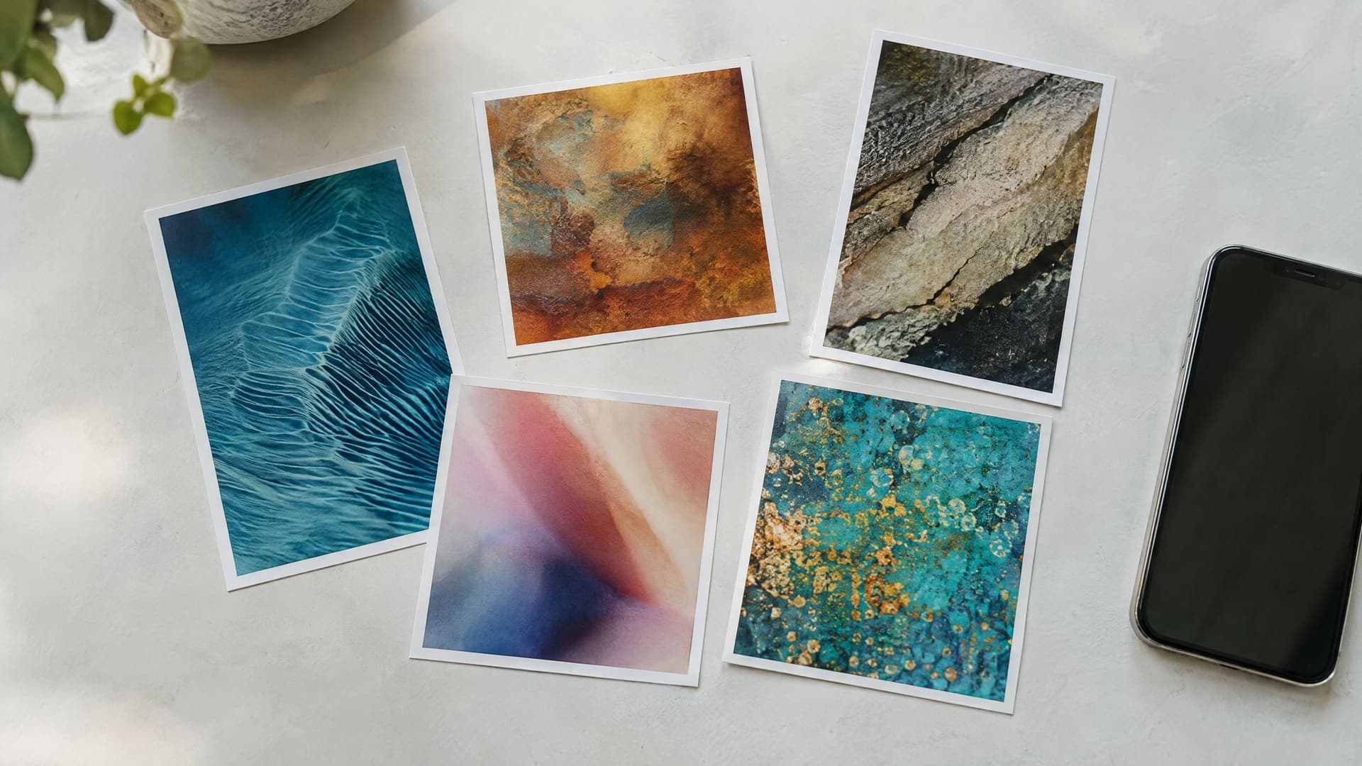 Mehrere ausgedruckte Fotos in Hochformat und Quadrat nebeneinander auf einem Tisch neben einem Smartphone, Motive abstrakt, keine Schrift