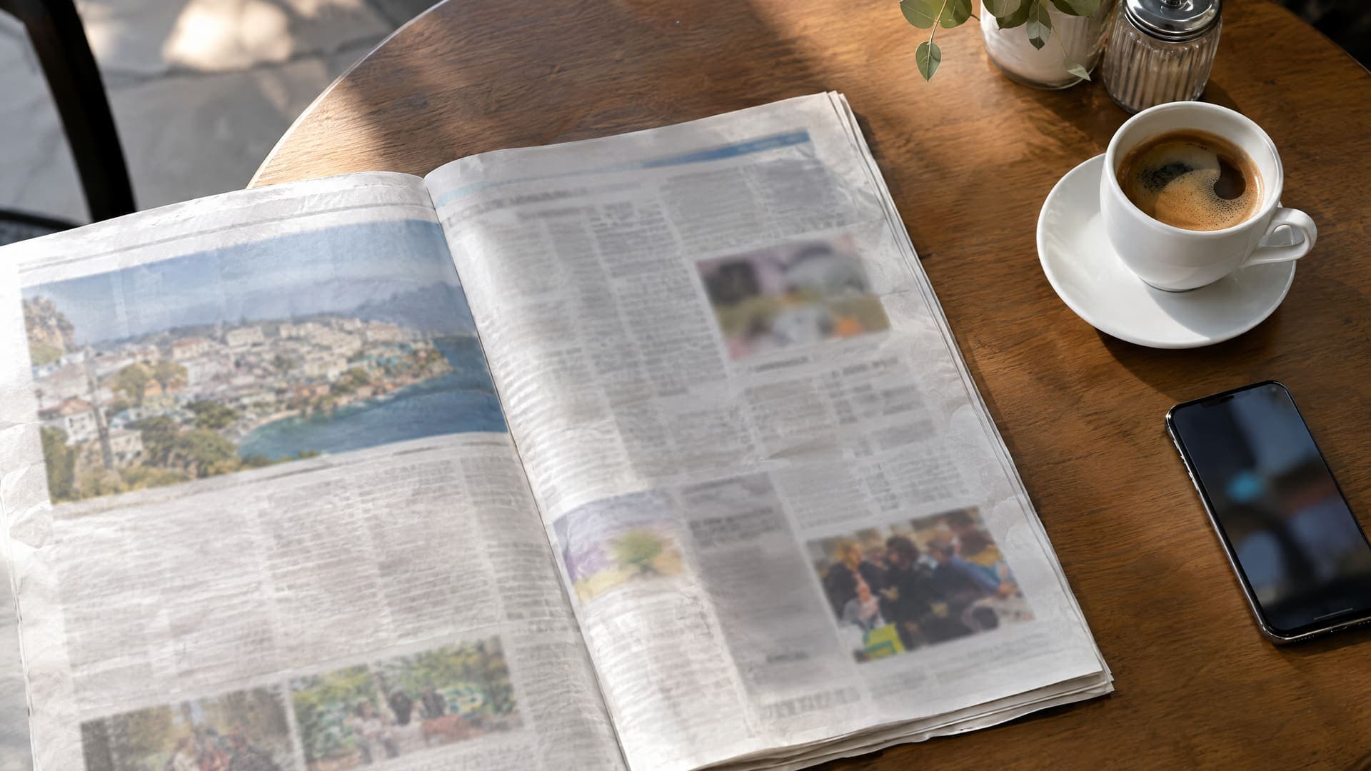 Aufgeschlagene Regionalzeitung mit unleserlichen Spalten auf einem Cafétisch neben einer Kaffeetasse im Morgenlicht, keine lesbare Schrift