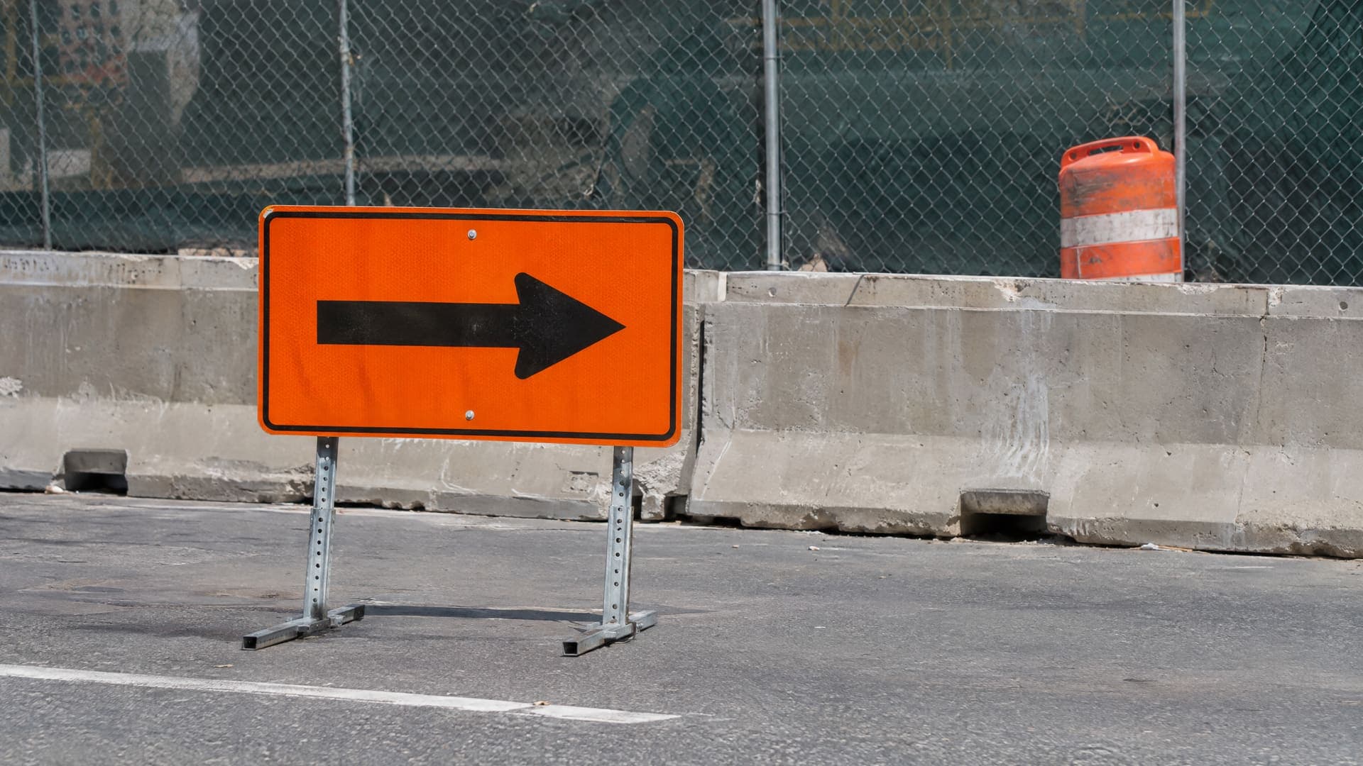 Orangefarbenes Umleitungsschild mit einem einzelnen Pfeil an einer Straße vor einer Baustellenabsperrung, Schild ohne Schrift