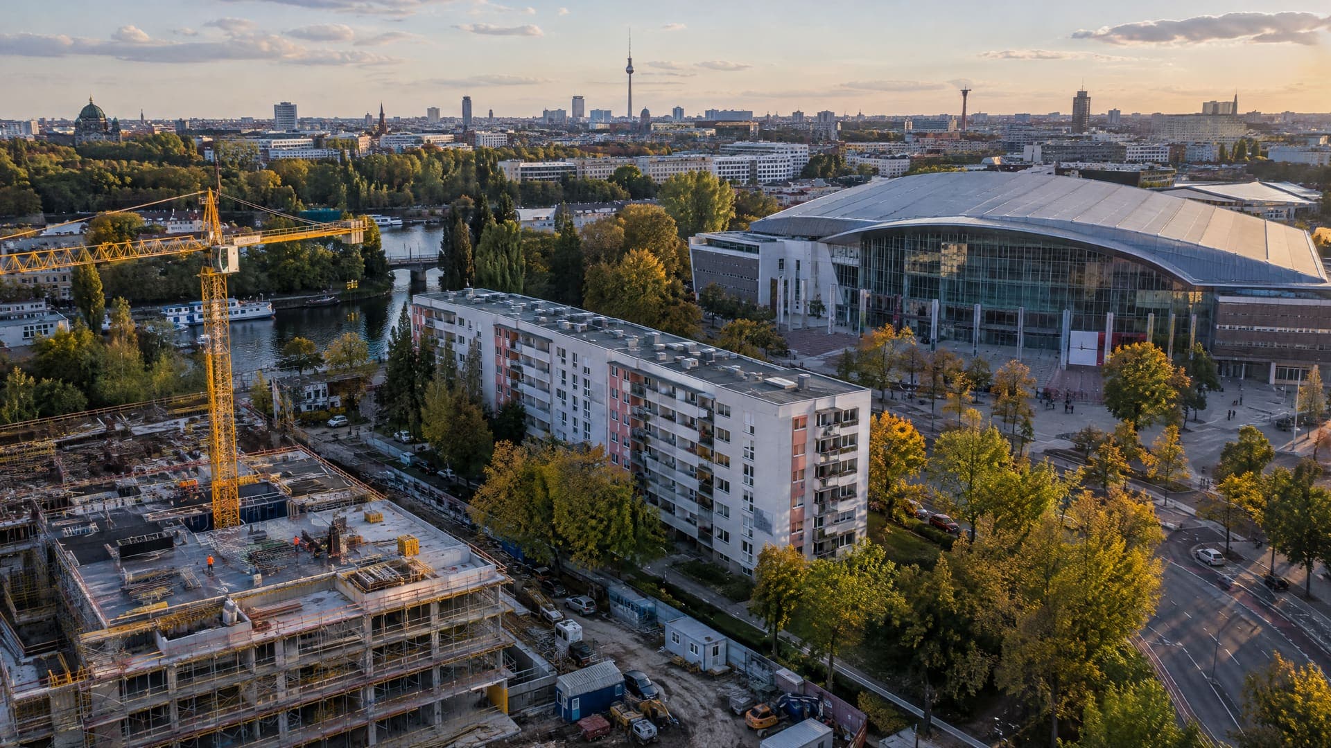 Luftbild eines Berliner Stadtquartiers mit Baustelle und Kran, Wohnblock und großer Veranstaltungshalle