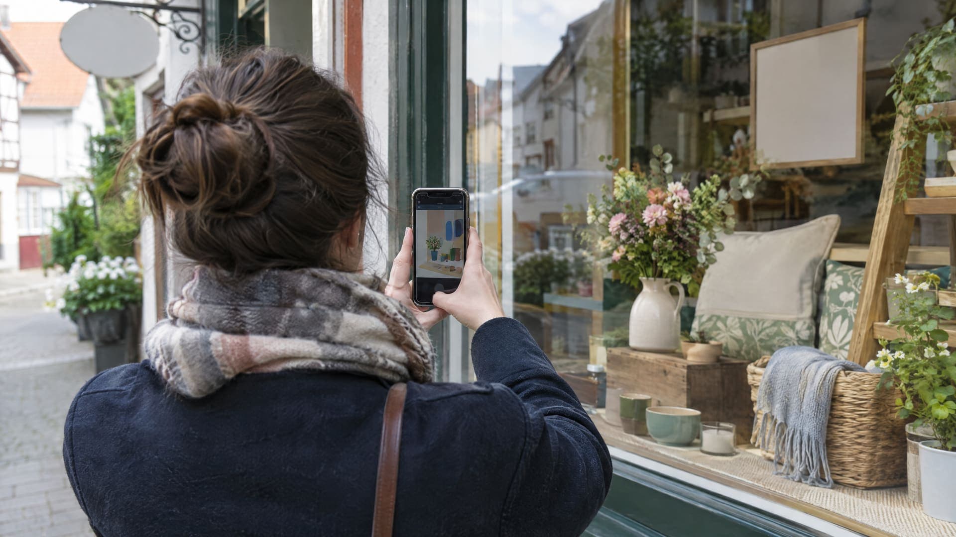 Person von hinten fotografiert mit dem Smartphone eine Auslage im Schaufenster eines kleinen Ladens, der Bildschirm zeigt nur abstrakte Formen