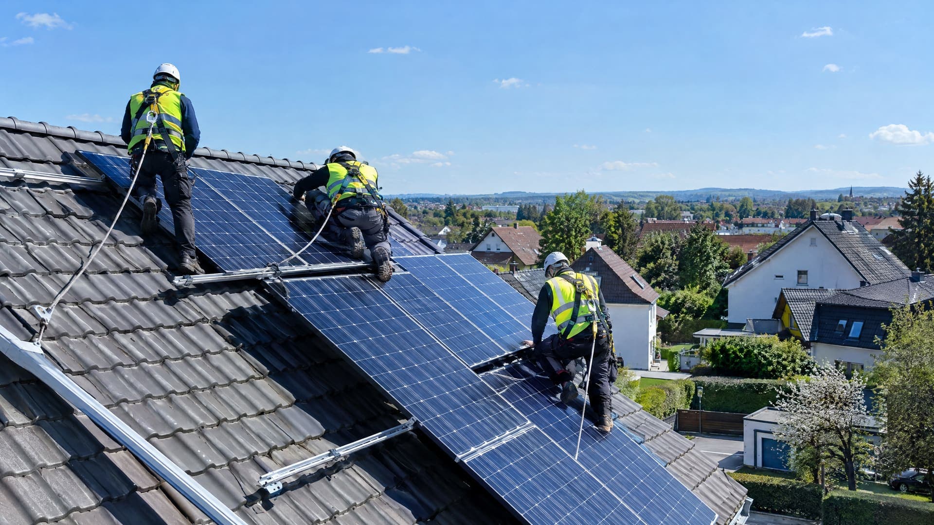 Installationsteam mit Helmen und Gurten montiert Photovoltaikmodule auf einem Dach