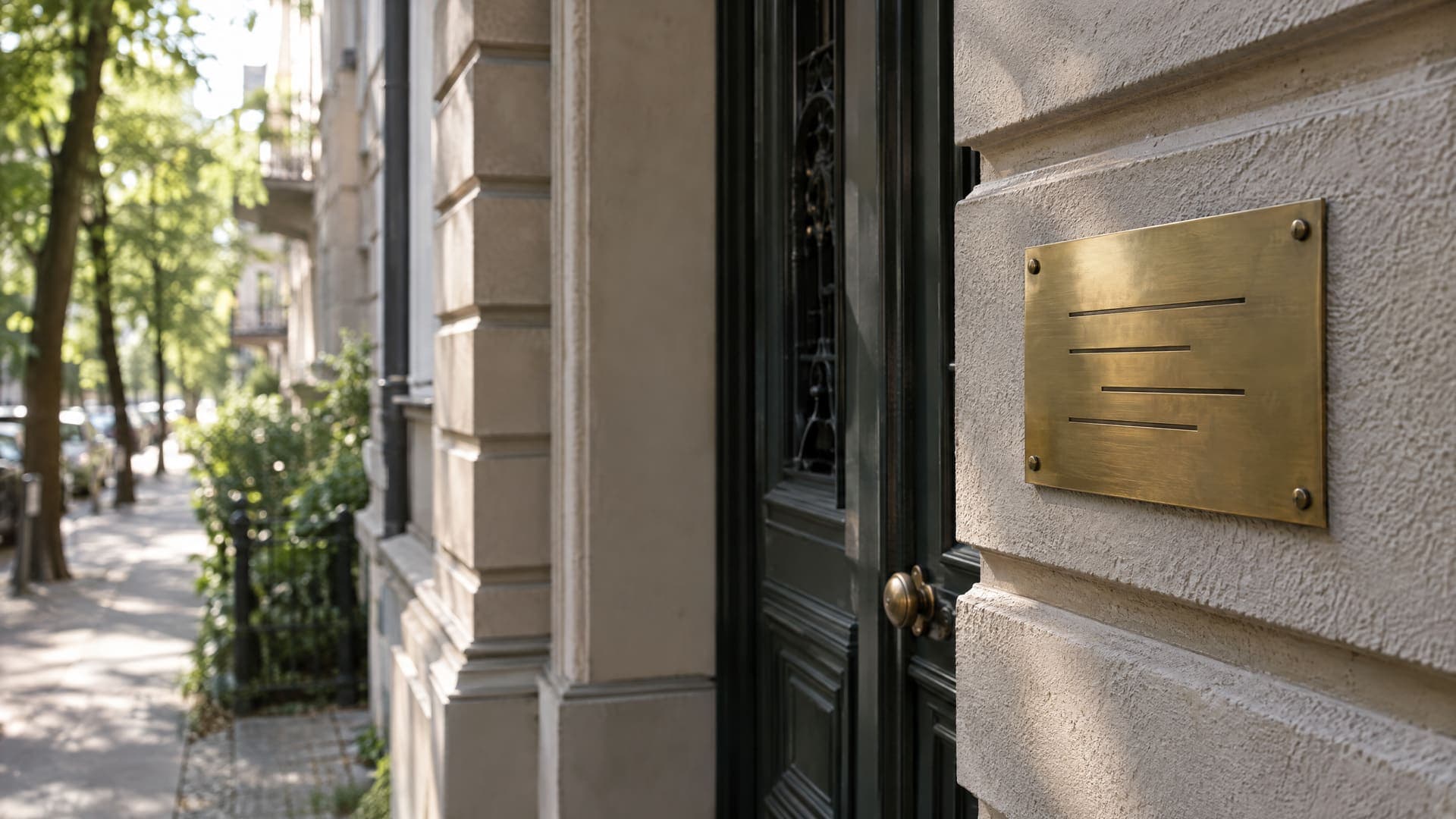 Schlichtes Praxisschild neben dem Eingang eines Berliner Altbaus im Morgenlicht, die Gravur ist nicht lesbar, Straßenbäume unscharf im Hintergrund