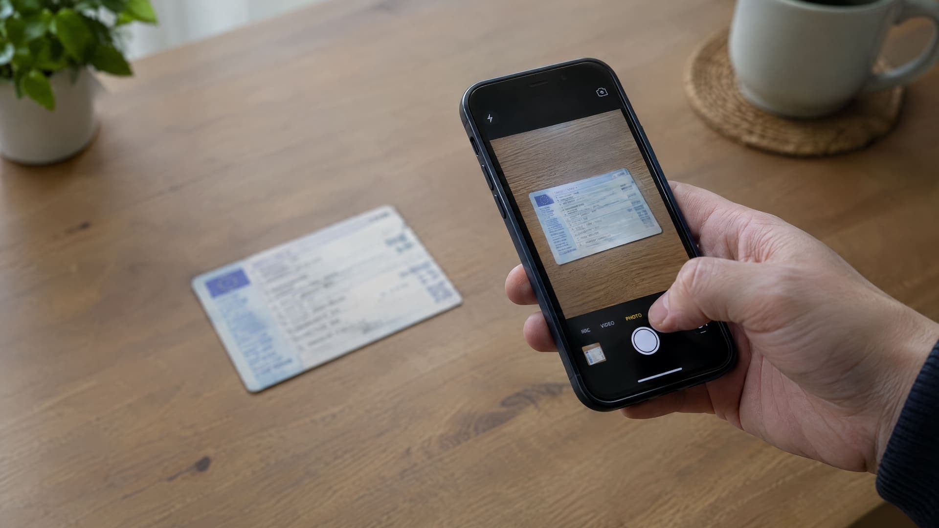 Hand fotografiert ein Fahrzeugdokument mit einem Smartphone auf einem Tisch, Schrift auf dem Dokument unleserlich