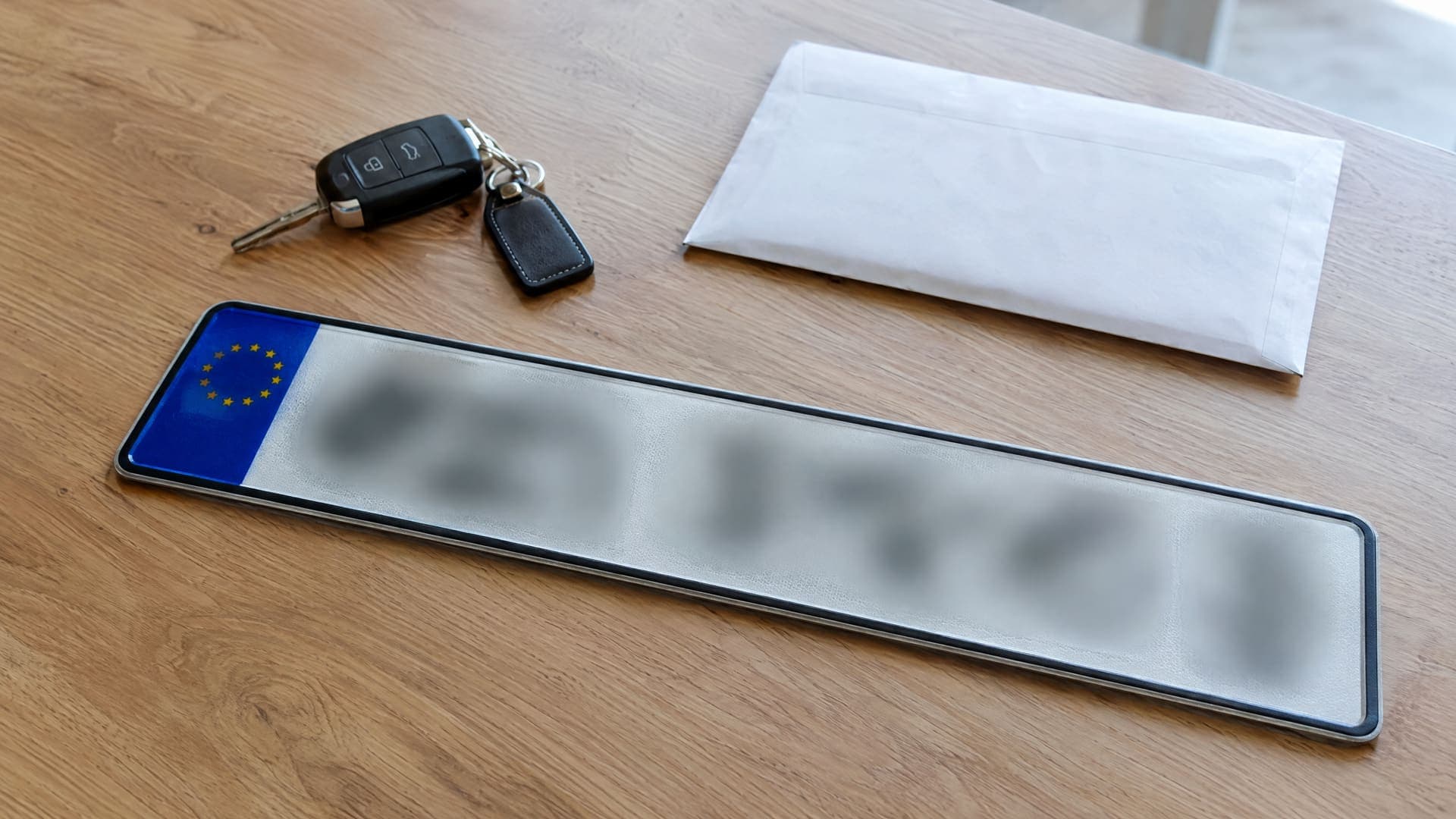 Kennzeichen mit unleserlichen Zeichen neben Autoschlüsseln und einem Umschlag auf einem Tisch